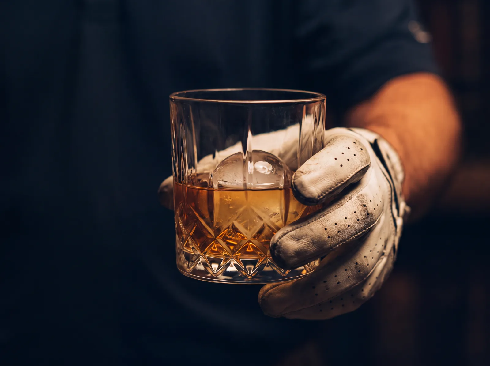 Whiskey in a cut-crystal glass, held in a golf glove